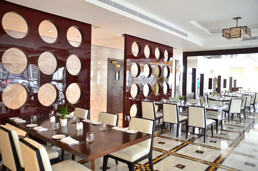 잔나 버즈 알 사라브 호텔 아부다비 외부 사진 The photo shows a modern restaurant interior. It features a series of tables with elegant place settings and comfortable chairs. The walls are decorated with a unique design, displaying round mirrors or circular elements set in a polished brown panel